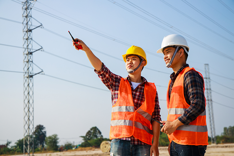 Asian engineer manager and foreman or leader discussion and pointing to construction site project on workplace and High voltage power line pylon in the background. Teamwork, Leadership concept.