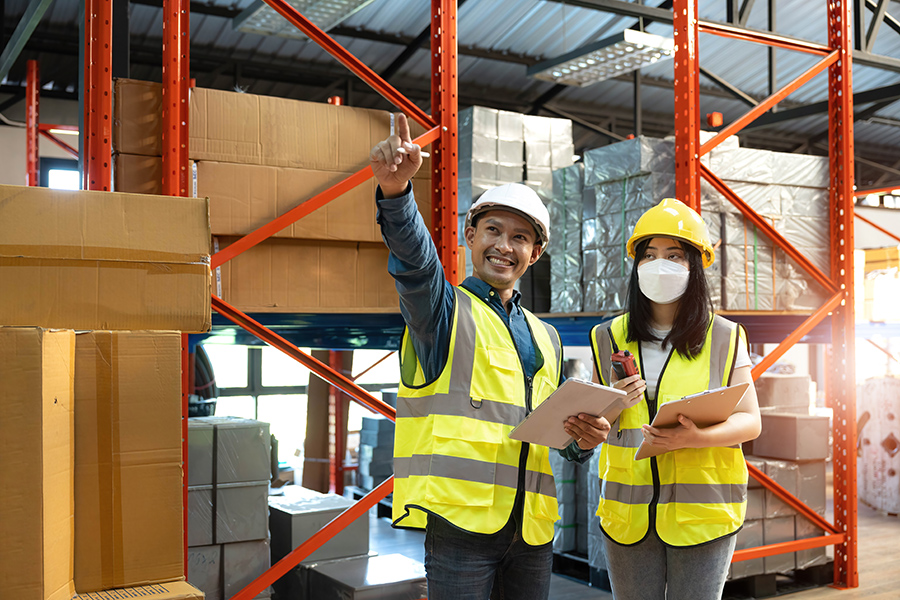 Professional adult Asian male warehouse manager and female worker are working together, checking their inventory in the warehouse or storehouse.